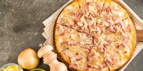 Flammekueche gourmande, garnie de lardons et d'oignons sur une base de fromage blanc crémeux. Un délice croustillant.