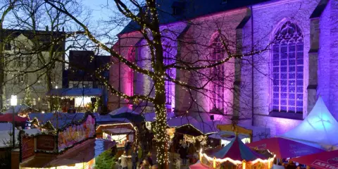 Bunte Lichter und Buden auf dem weihnachtsmarkt werne. Eine Kirche im Hintergrund erstrahlt in lila Licht.