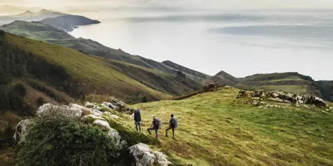 Trzech turystów podczas trekkingu na zielonym wzgórzu z widokiem na morze i góry.