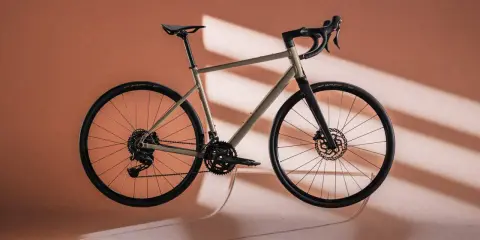 Ein Gravelbike in einem sanften Sandton, das wie ein Kunstwerk schwebt. Der Rahmen und die Reifen bilden einen harmonischen rose blend mit dem Hintergrund.