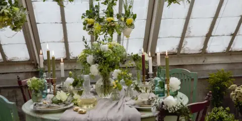 Vacker blomsterdekoration på bordet med levande ljus och gröna detaljer. En inbjudande dukning i ett växthus.