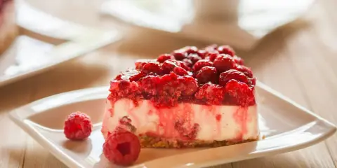 Pyszny sernikobrownie z malinami na białym talerzyku, ozdobiony świeżymi malinami.