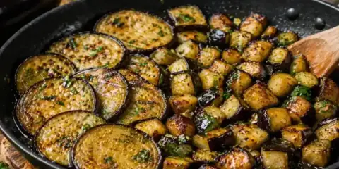 Aubergines au four, coupées en rondelles et en dés, dorées et parsemées d'herbes, dans une poêle. Un délice simple et savoureux.