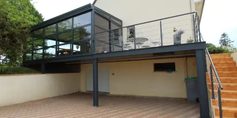 Modèle de véranda sur balcon avec structure métallique et vitrage. Un espace extérieur aménagé avec table et chaises.