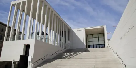 Moderne James-Simon-Galerie mit langer Treppe, ein Werk bekannter Architekten, vor blauem Himmel.