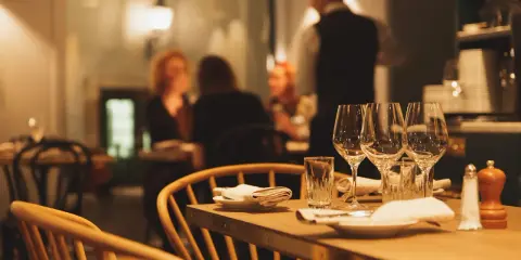 Ett dukat bord med vinglas och servetter, redo för en matvandring i Stockholm. I bakgrunden syns gäster och personal i en mysig restaurangmiljö.