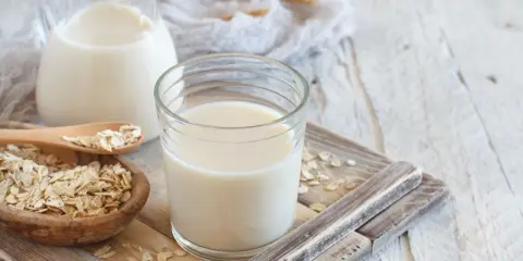 Szklanka i dzbanek z mlekiem owsianym, obok miseczka płatków owsianych. Idealne na zdrowe śniadanie, mleko 2 procent kcal.