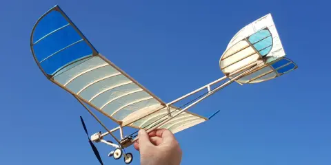 Ein handgefertigtes Modellflugzeug mit blau-weißen Flügeln, gehalten von einer Hand, bereit zum Flug. Ein echter slow flyer.