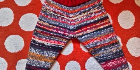 Pantalón de punto para bebé con rayas multicolores y cintura roja, sobre fondo de lunares.