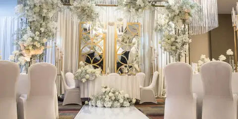 Eleganckie przyjęcie po ślubie cywilnym. Białe kwiaty, złote lustra i białe pokrowce na krzesłach tworzą romantyczną atmosferę.