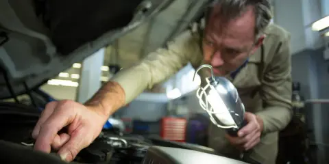 Mechanik sprawdza bezpieczniki w Grande Punto, używając lampy inspekcyjnej.