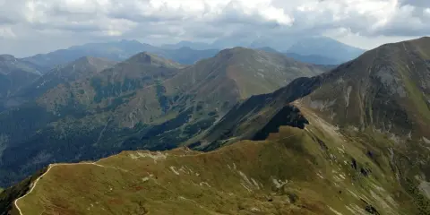 Widok na pasmo górskie, gdzie w Tatry prowadzi wydeptana ścieżka. Chmury na niebie.