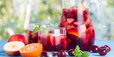 Une carafe et des verres de sangria rouge remplis de fruits frais, parfaits pour une recette de sangria rouge estivale.