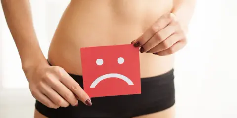 Kobieta trzyma kartkę z smutną buźką, symbolizującą krwawienie po stosunku.