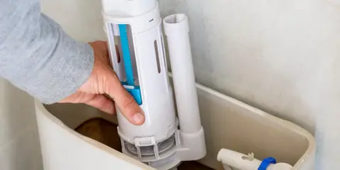 Mano instalando el mecanismo de descarga, una de las partes de una cisterna de baño. Se ve el flotador y la tubería de llenado.