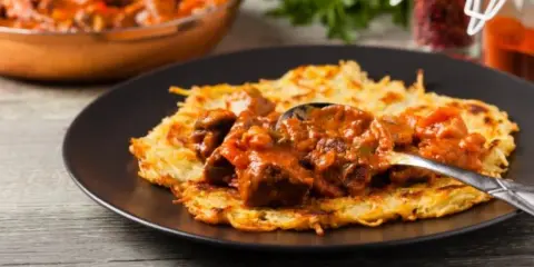 Gęsty, aromatyczny sos do placków ziemniaczanych z kawałkami mięsa i warzyw, podany na chrupiących plackach.