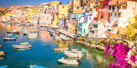 Porto di Corricella a Procida, un gioiello colorato. Ecco cosa vedere a Procida in un giorno: case pastello, barche nel blu intenso e bouganville in fiore.