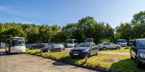 Na parkingu przy zamku Bolków stoi kilka samochodów i autobusów.