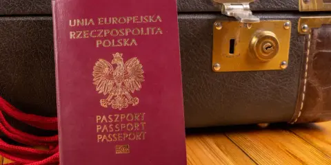 Polski paszport i brązowa walizka na drewnianym tle.