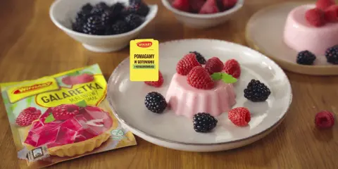 Panna cotta z malinami i jeżynami, obok opakowanie galaretki malinowej.
