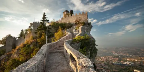 Sentiero in pietra che sale verso la Rocca della Guaita, simbolo di San Marino città, con vista panoramica sulla valle.