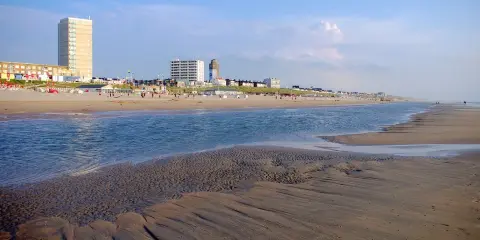 Piękny dzień nad morzem w Holandii. Piaszczysta plaża, spokojna woda i nowoczesne budynki w tle tworzą malowniczy krajobraz.