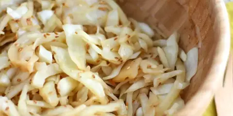 Salade de chou râpé assaisonnée de graines de sésame, servie dans un bol en bois.