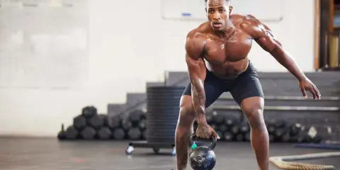 Ein Mann mit starkem Muskelaufbau hebt eine Kettlebell. Seine Anstrengung spiegelt die Ergebnisse von intensiven Trainingseinheiten wider, wie sie in Studien zum Muskelaufbau untersucht werden.