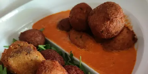 Polpette di pane dorate e croccanti, servite su una salsa rossa cremosa e guarnite con rucola fresca.
