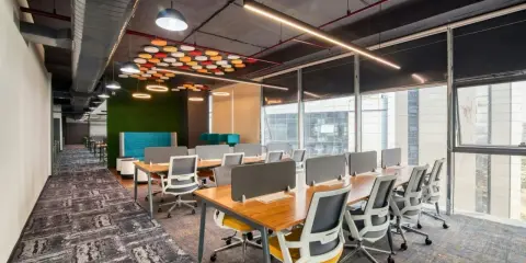 Nowoczesne biuro z rzędami biurek, zieloną ścianą i designerską lampą biurową wiszącą nad stołem.