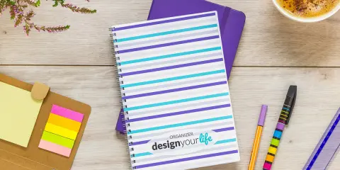 Pomysł na kalendarz: kolorowy notatnik z napisem "design your life", obok długopisy, karteczki i kawa.