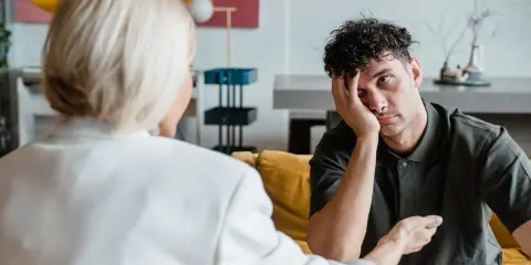 Mężczyzna w gabinecie neuropsychologa, oparty o dłoń, z wyrazem zmęczenia na twarzy.