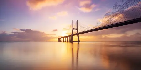 Ponte sospeso sull'acqua calma, con un cielo colorato da un tramonto mozzafiato. Una foto da fare al tramonto, perfetta per catturare la magia del momento.