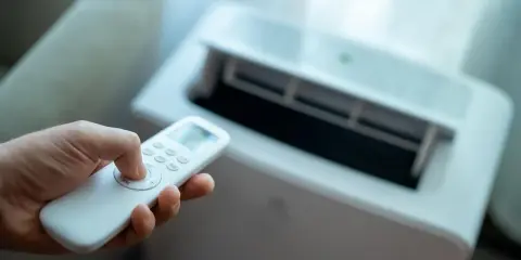Main tenant utilise la télécommande pour régler son meilleur climatiseur mobile pas cher.
