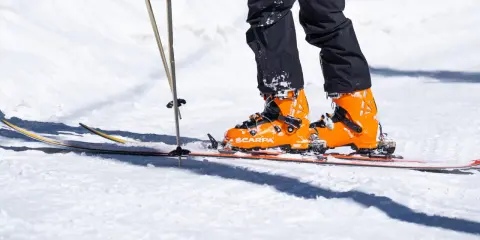 Pomarańczowe buty narciarskie Scarpa na nartach, z kijkami narciarskimi w śniegu.