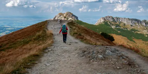 Szlak na czerwone wierchy z Kuźnic. Turystka z plecakiem idzie kamienistą ścieżką wśród traw.