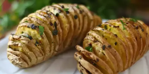 Två gyllene hasselbackspotatisar med örter, redo att serveras. Ett perfekt hasselbackspotatis recept för middagen.