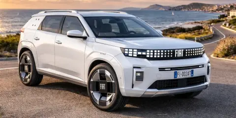 Un'imponente Fiat, quasi un giga panda, sfreccia su una strada costiera al tramonto.