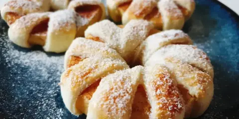 Pyszne ciasto francuskie z jabłkami, posypane cukrem pudrem, prezentuje się apetycznie na granatowym talerzu.
