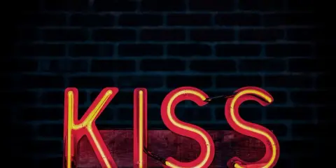 Neonowy napis KISS na tle ceglanej ściany. Zasada KISS: Keep It Simple, Stupid.