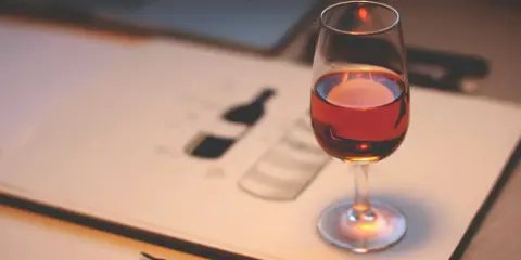 Ein Glas Portwein steht auf einem Skizzenbuch, das eine Flasche zeigt. Perfekt, um zu lernen, wie trinkt man Portwein.