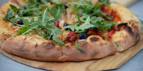 Idealne ciasto na pizzę z rukolą, oliwkami i papryką, wypieczone na drewnianej desce.