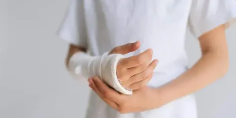 Dziecko z opuchlizną po zdjęciu gipsu nadgarstek, w białej koszulce, z ręką owiniętą bandażem.