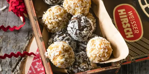 Leckere energy balls selber machen! Eine Mischung aus dunklen und hellen Kugeln, umhüllt von Kokosraspeln, in einer alten Blechdose.