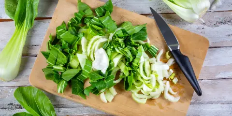 Frischer Pak Choi wird auf einem Holzbrett zerteilt, bereit zum Zubereiten. Ein Messer liegt daneben.