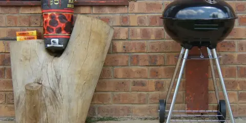 Grill stoi w bezpiecznej odległości od budynku, obok drewnianego pnia z węglem.