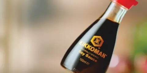 Butelka sosu sojowego Kikkoman z czerwoną zakrętką na drewnianym blacie.