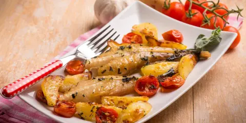 Pyszny mintaj z piekarnika podany z pieczonymi ziemniakami i pomidorkami koktajlowymi.