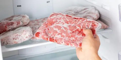 Ręka wyjmuje z zamrażarki worek z mrożonym mięsem. To idealny sposób, w czym mrozić mięso, by zachować jego świeżość.