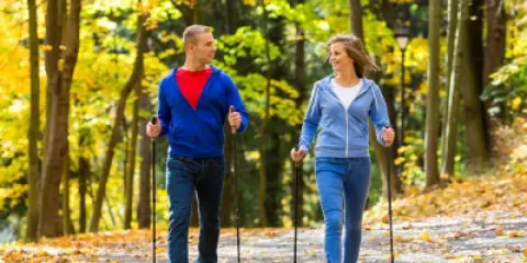 Para spacerująca z kijkami w jesiennym parku. Uczą się, jak chodzić z kijkami, ciesząc się złotymi liśćmi.